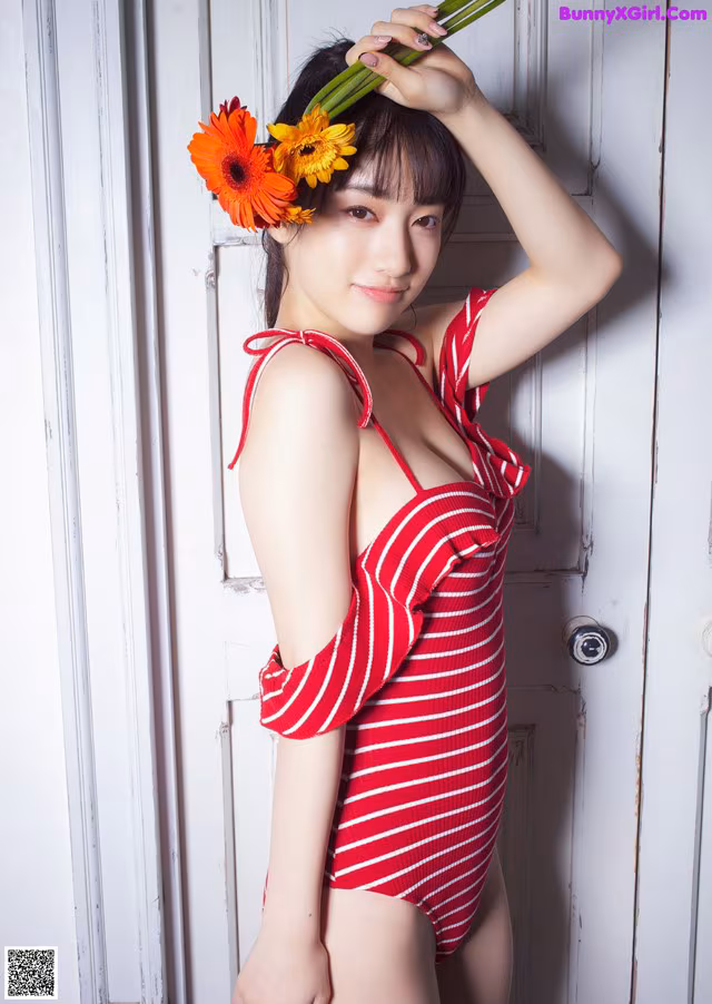 A woman in a red and white striped bathing suit holding a flower.