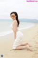 A woman in a white dress and sunglasses on the beach.