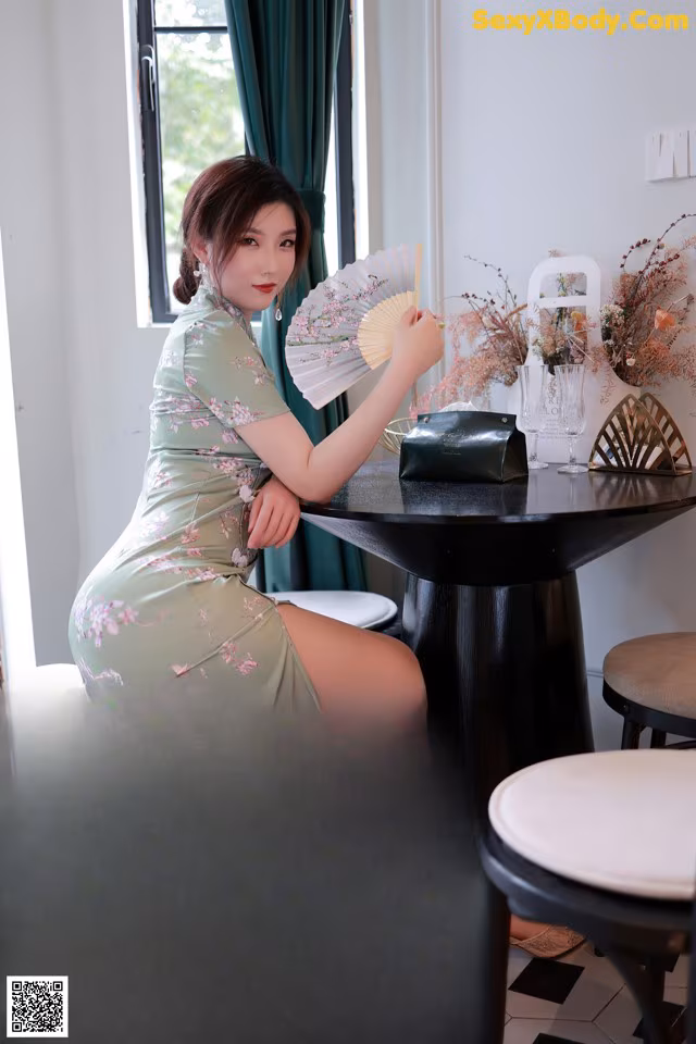 A woman sitting at a table holding a fan.