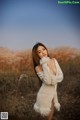 A woman in a white sweater standing in a field.