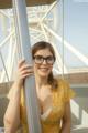 A woman wearing glasses leaning against a pole.