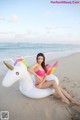 A woman in a pink bikini sitting on an inflatable unicorn on the beach.