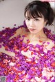 A woman laying in a bathtub filled with pink and purple petals.