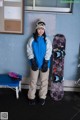 A woman standing next to a snowboard in front of a wall.