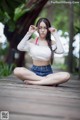 A woman sitting on a wooden boardwalk wearing glasses.