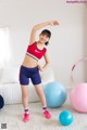 A woman in a red sports bra top and blue shorts posing for a picture.